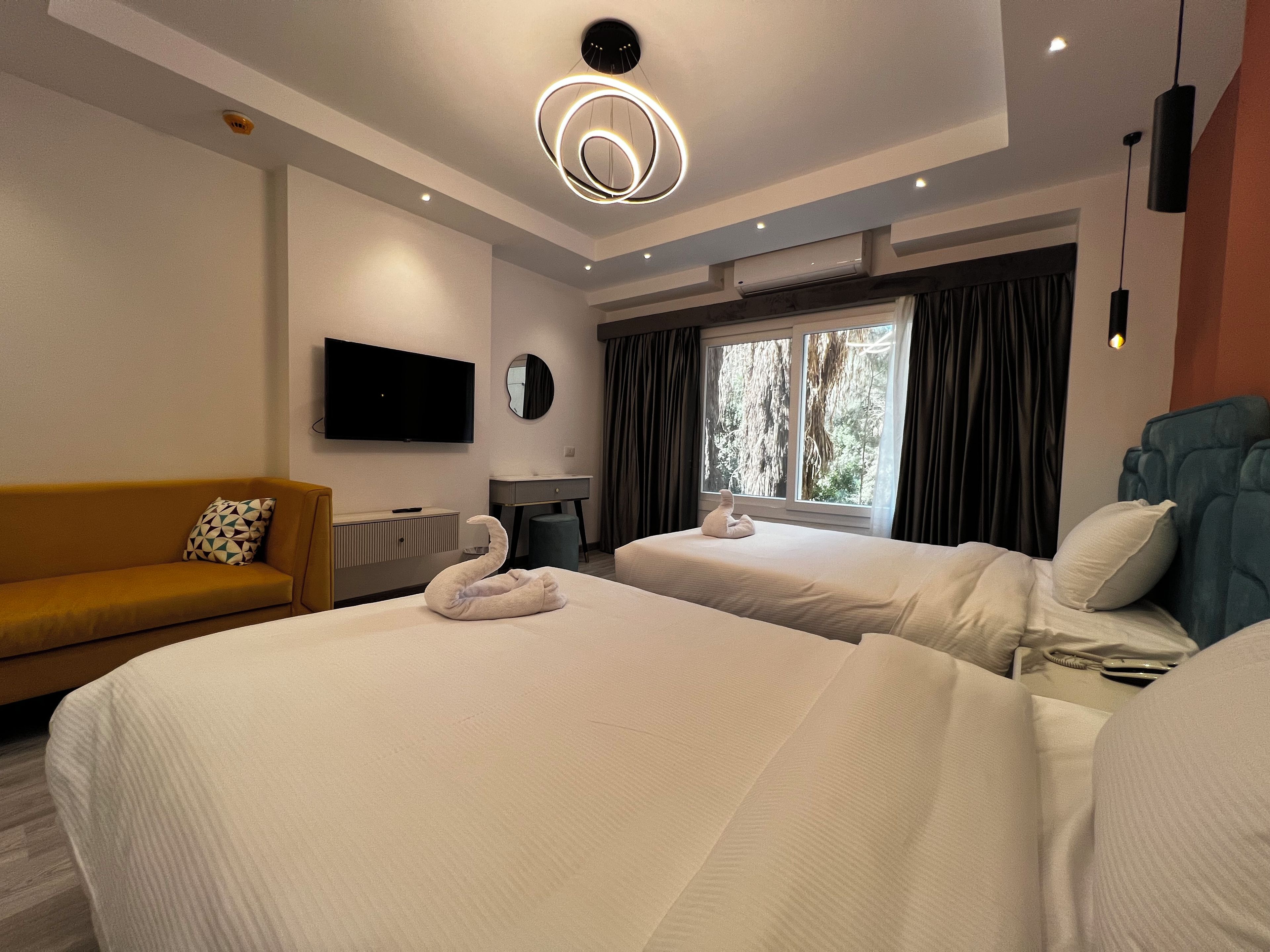 Hotelkamer met twee bedden, een slaapbank, een flatscreen televisie, een spiegel en een raam met gordijnen.