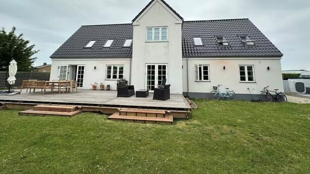 Ein zweistöckiges Haus mit flachem Dach, großen Fenstern und einer Terrasse mit Gartenmöbeln.