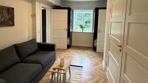 Ein Wohnzimmer mit einer Couch, einem Couchtisch, einem Teppich und einem Fenster mit Blick auf Grünflächen.