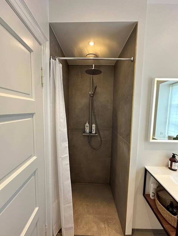 A compact shower area with a ceiling light, a showerhead, and a shelf with toiletries.