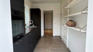 Eine moderne Küche mit dunklen Schränken, einem eingebauten Backofen und einer Spüle aus Edelstahl.