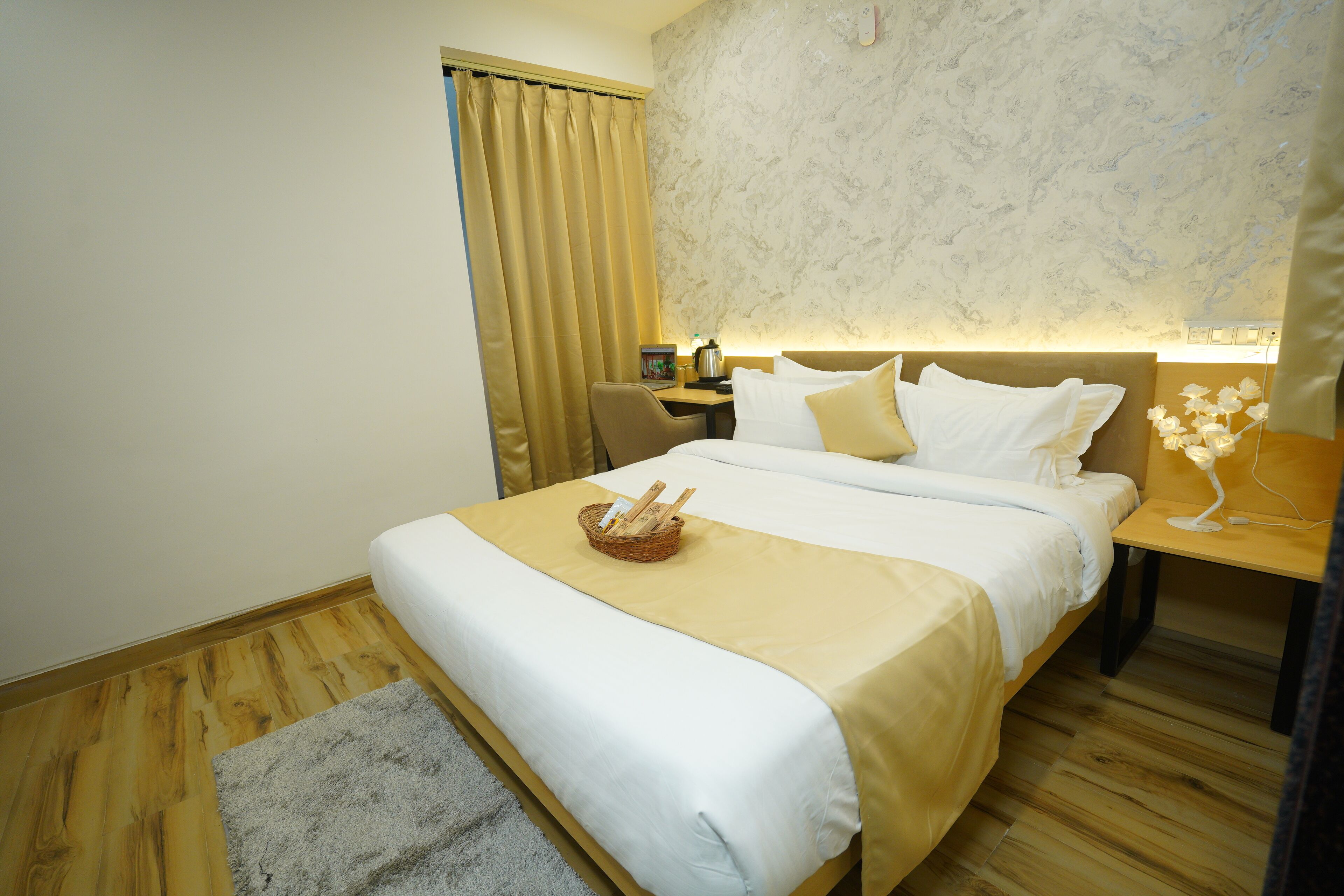 A hotel room with a large bed, a desk with a lamp, a chair, and a small table with a decorative item.