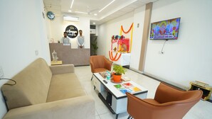 A reception area with a reception desk, a sofa, two chairs, a coffee table with a plant, and a TV mounted on the wall. - Anugya - A Boutique Hotel (Indore)