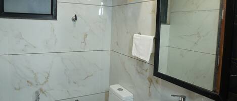 A bathroom with a white toilet, a sink, a mirror, and a shower.