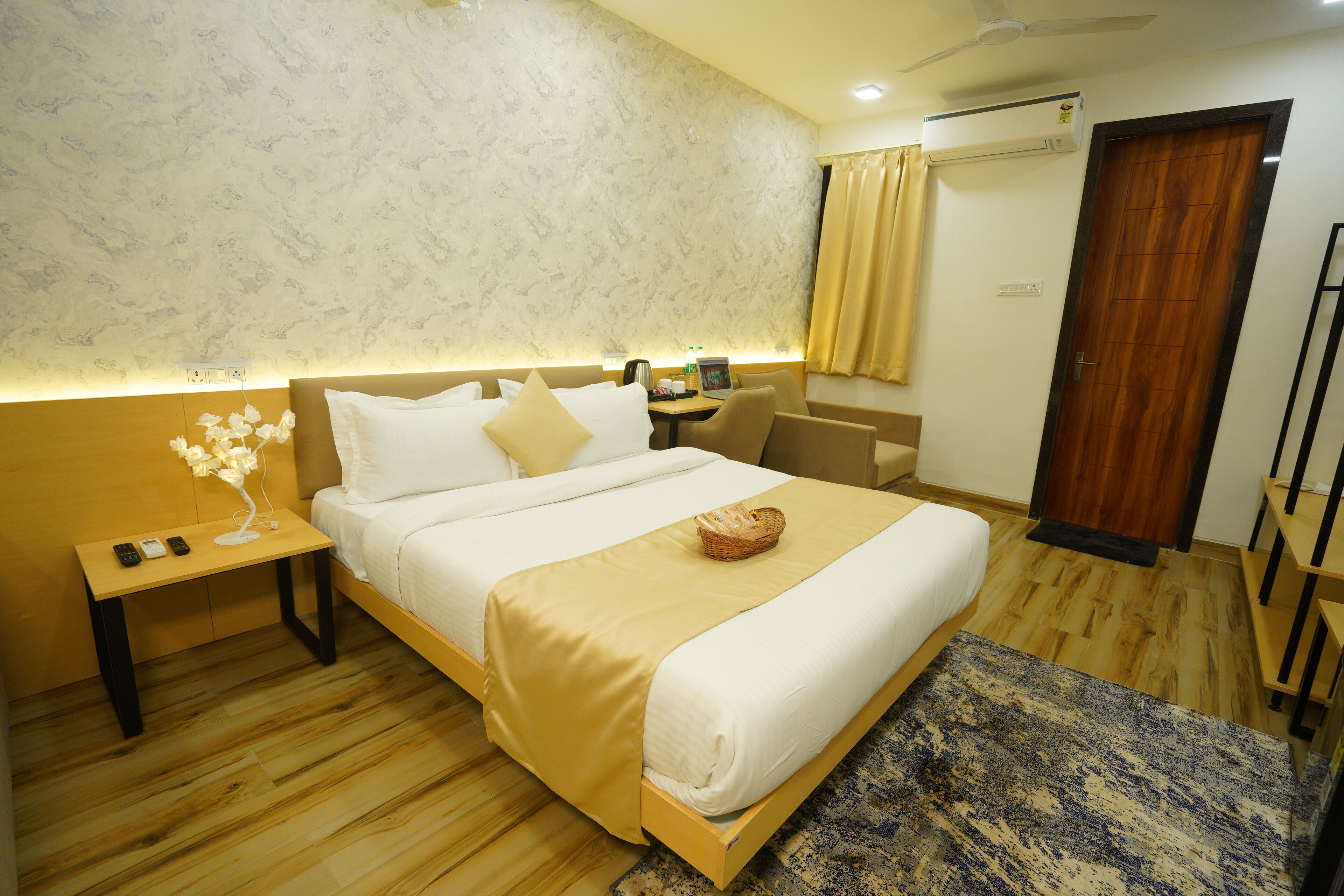 A hotel room with a bed, bedside table, lamp, and a small table with a laptop.