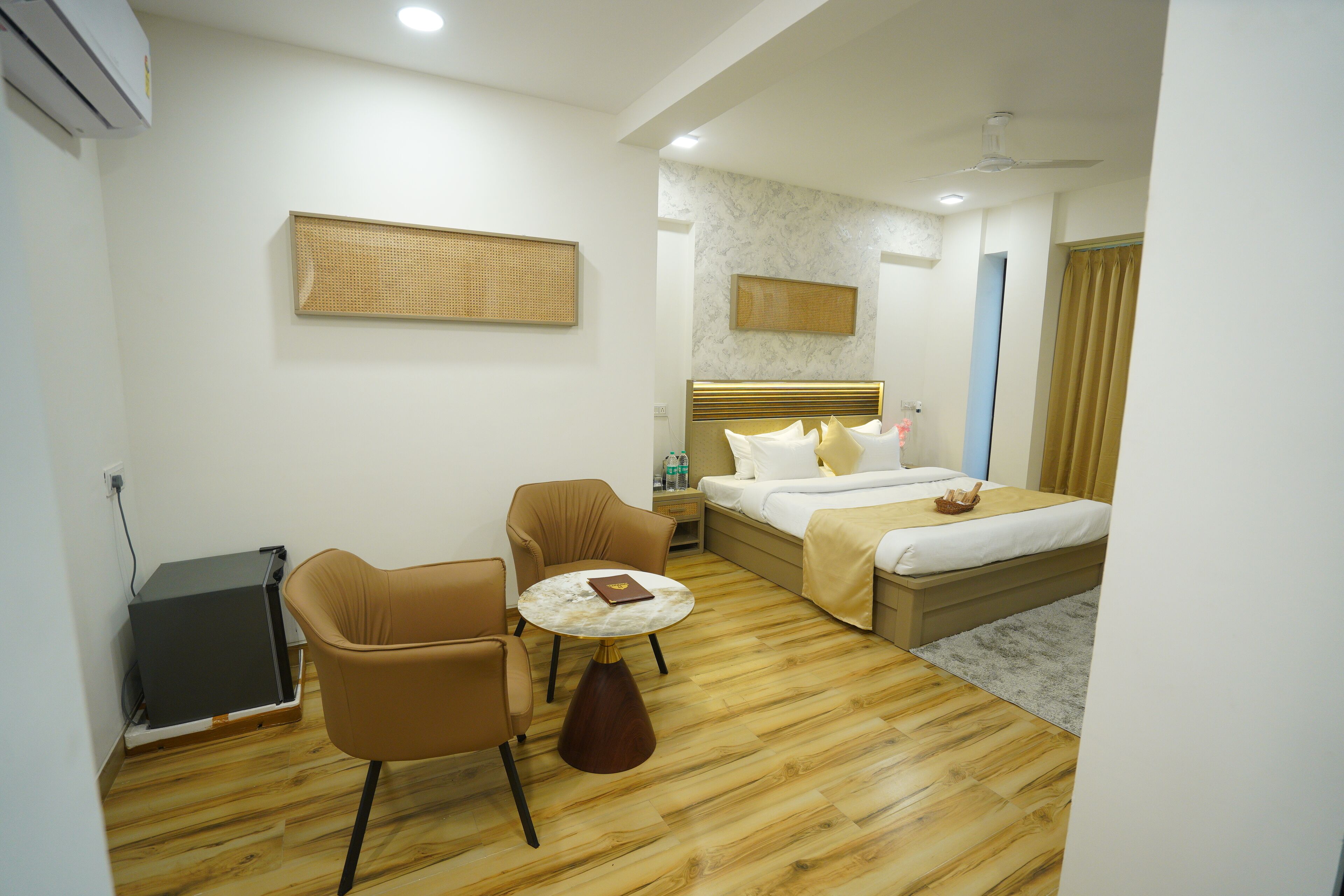 A hotel room with a bed, two chairs, a small table, a nightstand, and a wall-mounted TV.