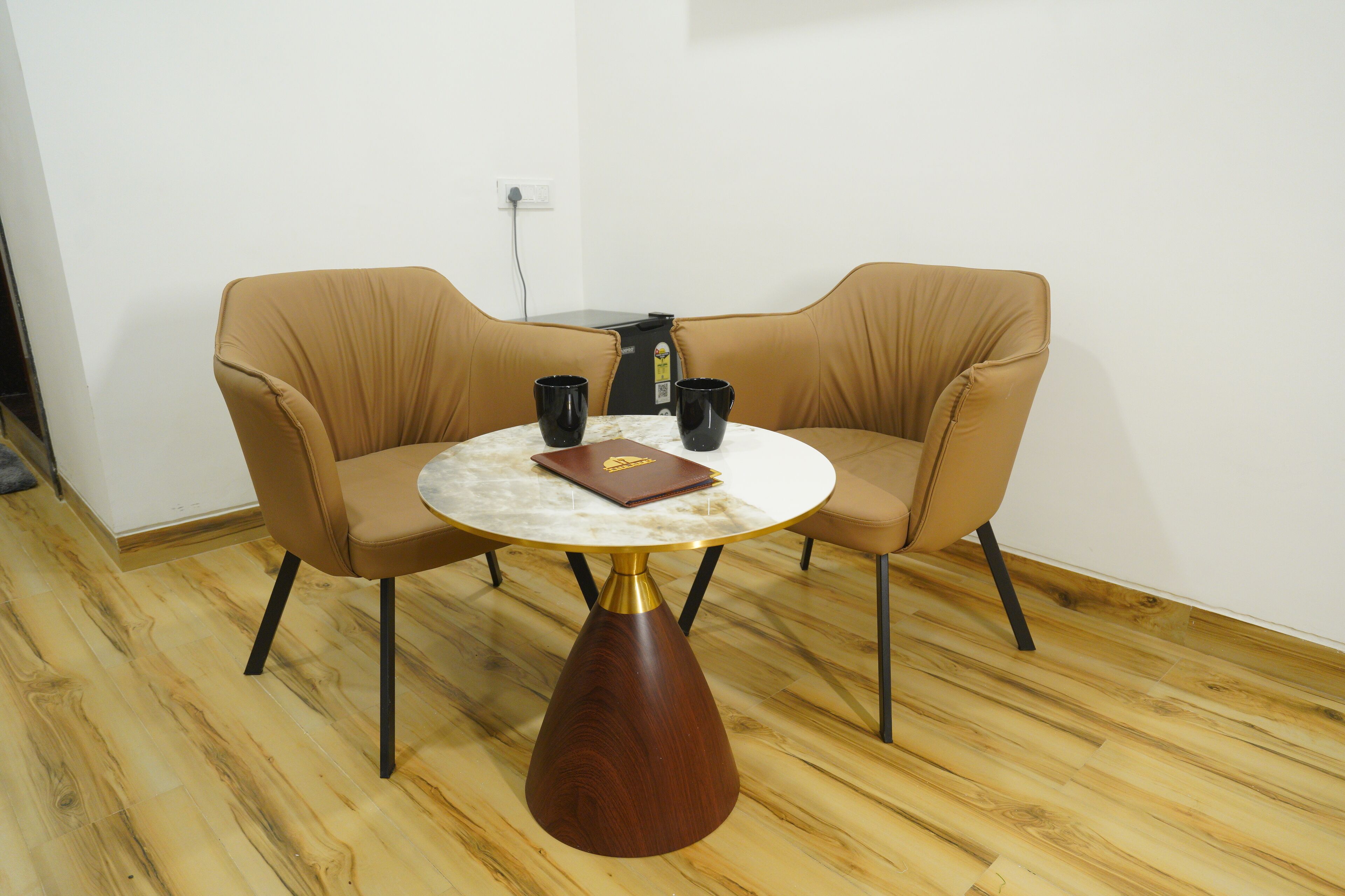 Une pièce avec une table ronde, deux fauteuils en cuir marron et deux tasses noires posées sur la table.