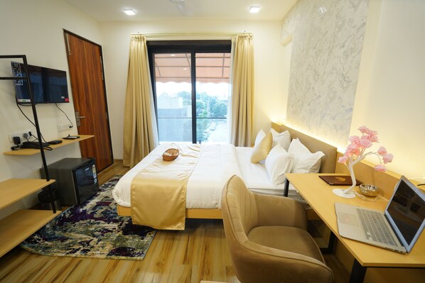 A hotel room with a bed, a desk with a laptop, a chair, a TV, and a window with curtains. - Anugya - A Boutique Hotel (Indore)