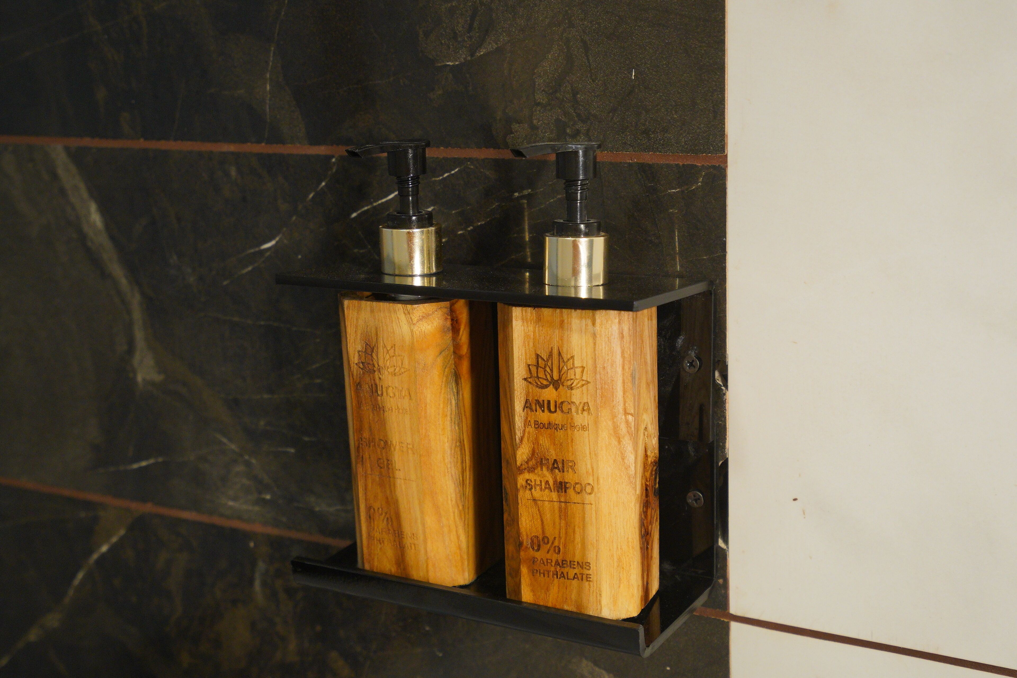 Two wooden dispensers with pumps on a black shelf against a dark marble wall.