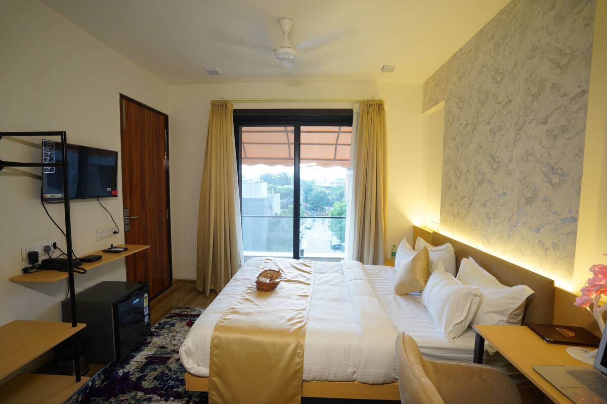 Una habitación de hotel con cama, escritorio y televisor sobre una estantería.