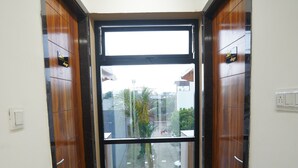 A hallway with a glass door leading to an outdoor area, wooden doors on either side, and a potted plant near the entrance. - Anugya - A Boutique Hotel (Indore)