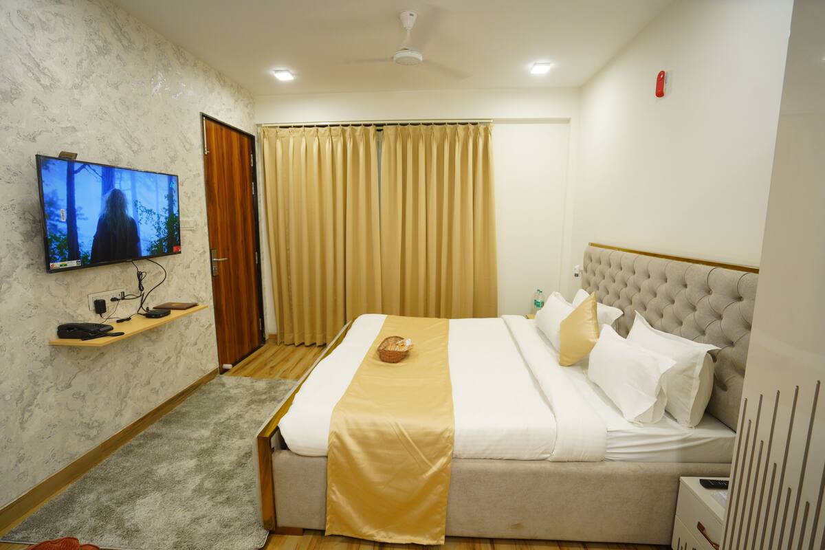 Habitación de hotel con una cama, televisor, estante de madera, ventana con cortinas y ventilador de techo.