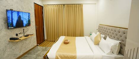 A hotel room with a bed, a television, a wooden shelf, a window with curtains, and a ceiling fan.