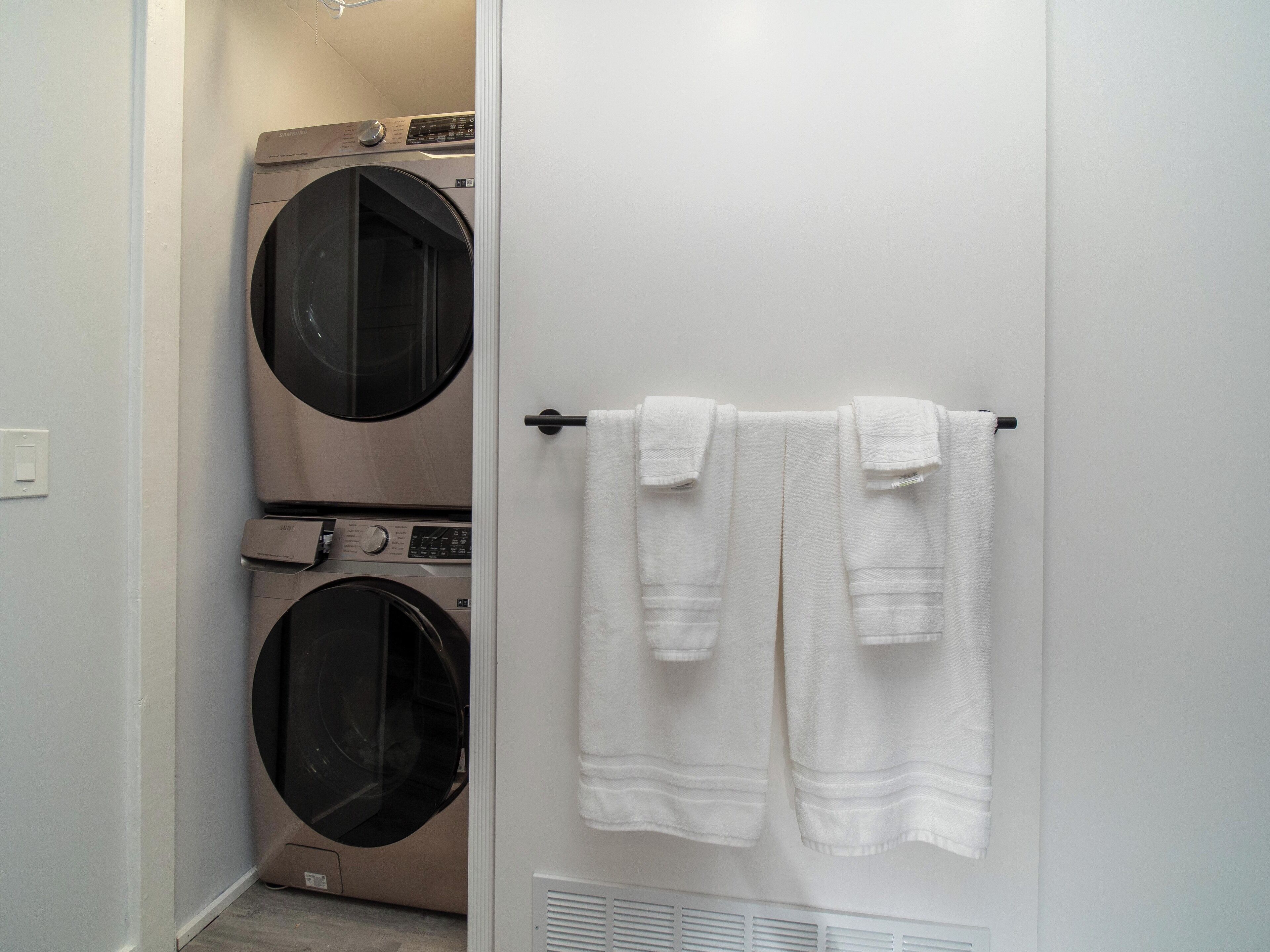 A laundry room with two stacked front-loading washers and dryers, a towel rack with two towels, and a white door.
