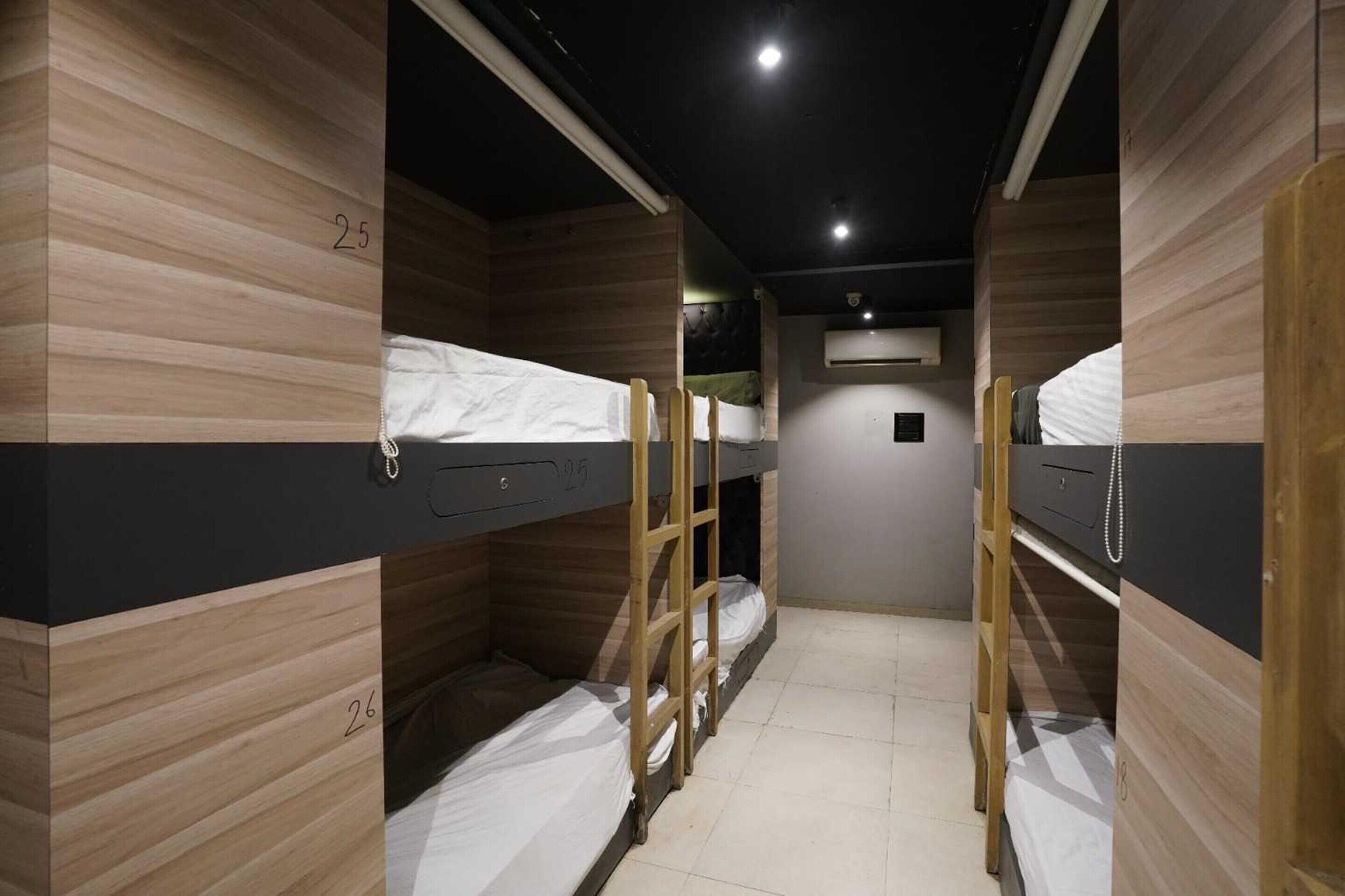 A dormitory room with bunk beds, numbered 25 and 26, wooden walls, and a ceiling light.