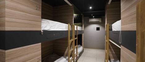 A dormitory room with bunk beds, numbered 25 and 26, wooden walls, and a ceiling light.