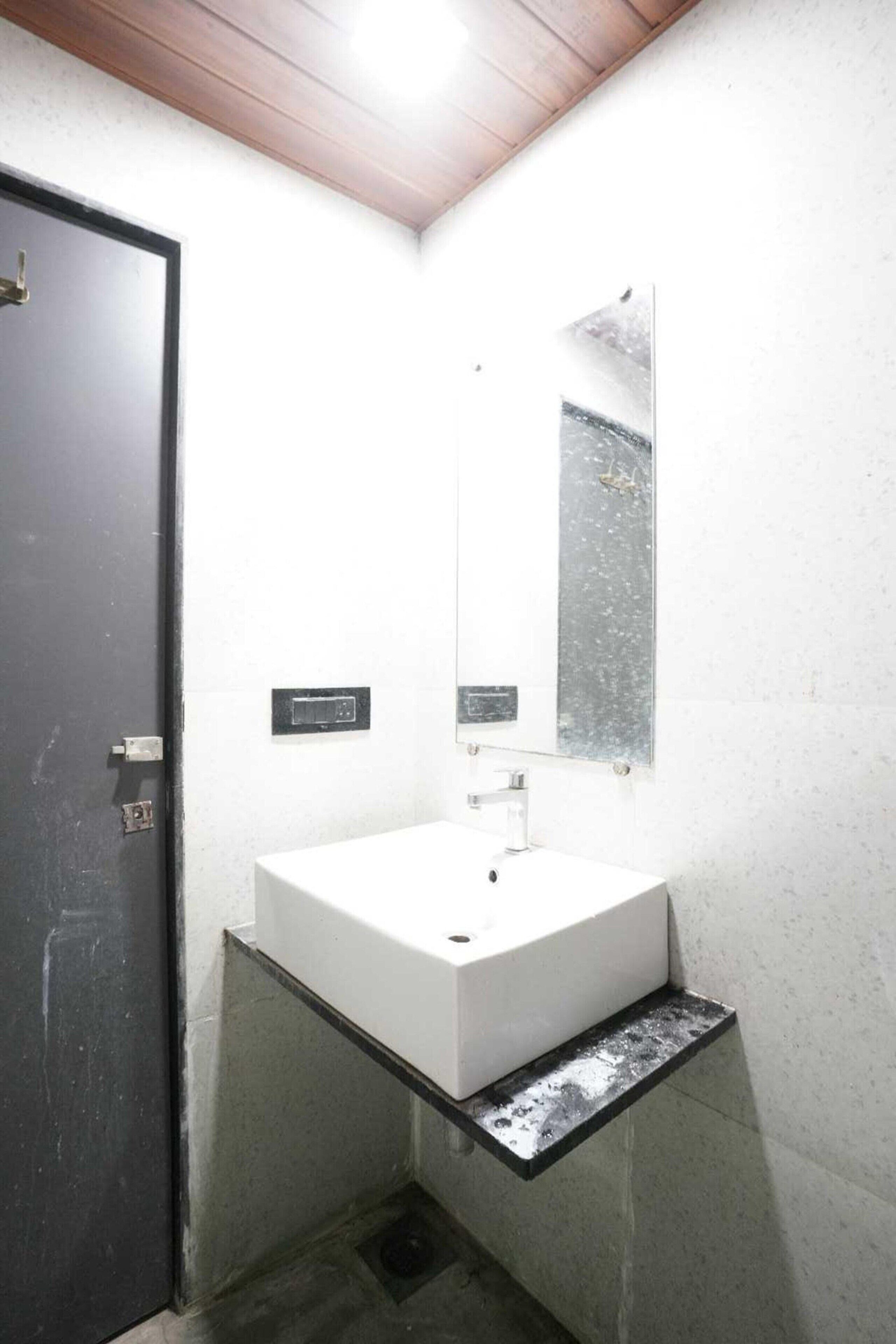 A small, modern bathroom with a white sink, a mirror, and a black door.