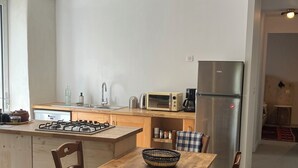Een moderne keuken met een houten eettafel, twee stoelen, een gasfornuis, een magnetron en een koelkast.