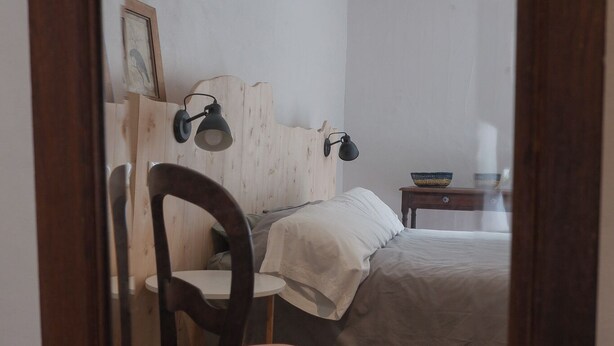 Een slaapkamer met een bed, een stoel, een nachtkastje en een lamp.