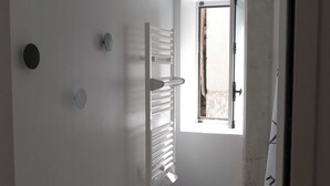 Een kleine, smalle kamer met witte muren, een raam met uitzicht en een handdoekhouder.