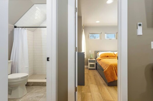 A modern bathroom with a shower, toilet, and a small bedside table with a lamp. - Cozy 1-bedroom MIL - fresh, clean and great location! (Denver)