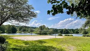 A grassy area with a volleyball net, trees, and a body of water in the background. - Charming Family Friendly House, Hot tub, Playroom (Long Pond)