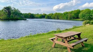 A picnic table by a lake with grassy banks and trees in the background. - Charming Family Friendly House, Hot tub, Playroom (Long Pond)
