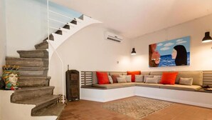Ein Wohnzimmer mit einer geschwungenen Treppe, einem Ecksofa, einem Gemälde und einem gemusterten Teppich.