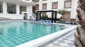 A swimming pool with blue lounge chairs, a stone wall, and a building with large windows and a staircase.