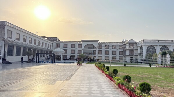A large, multi-story hotel with a central courtyard, a covered walkway, and a well-maintained lawn.