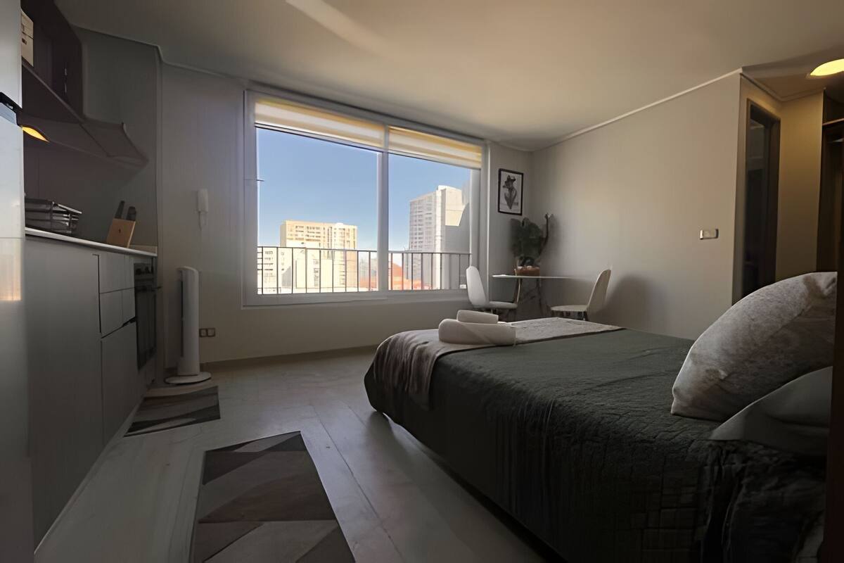 A modern bedroom with a large window, a bed, a desk, and a chair.