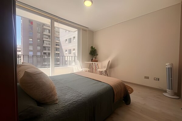 A bedroom with a bed, a small table with chairs, a potted plant, and a radiator.