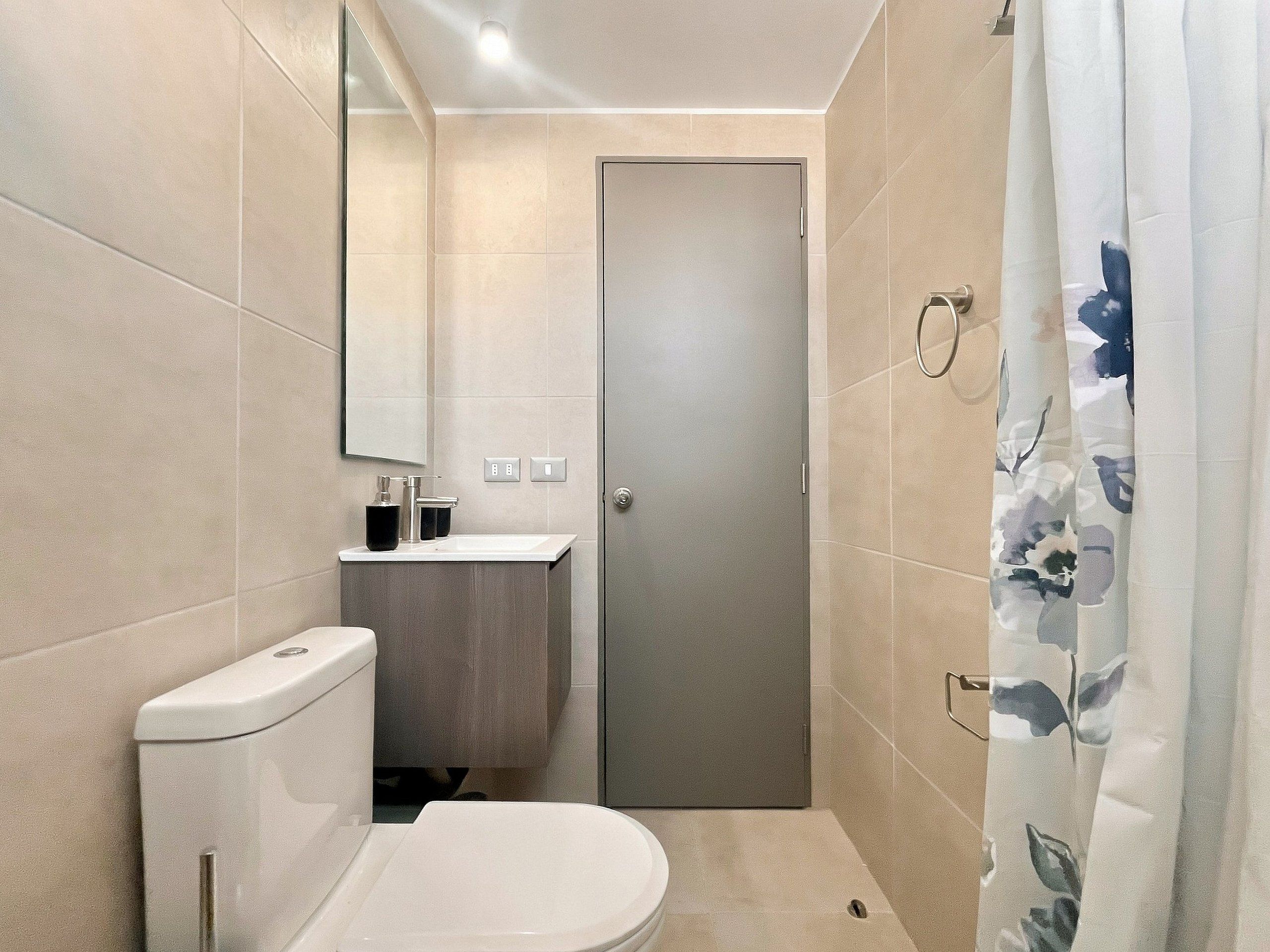 A compact bathroom with a toilet, sink, and a shower curtain.