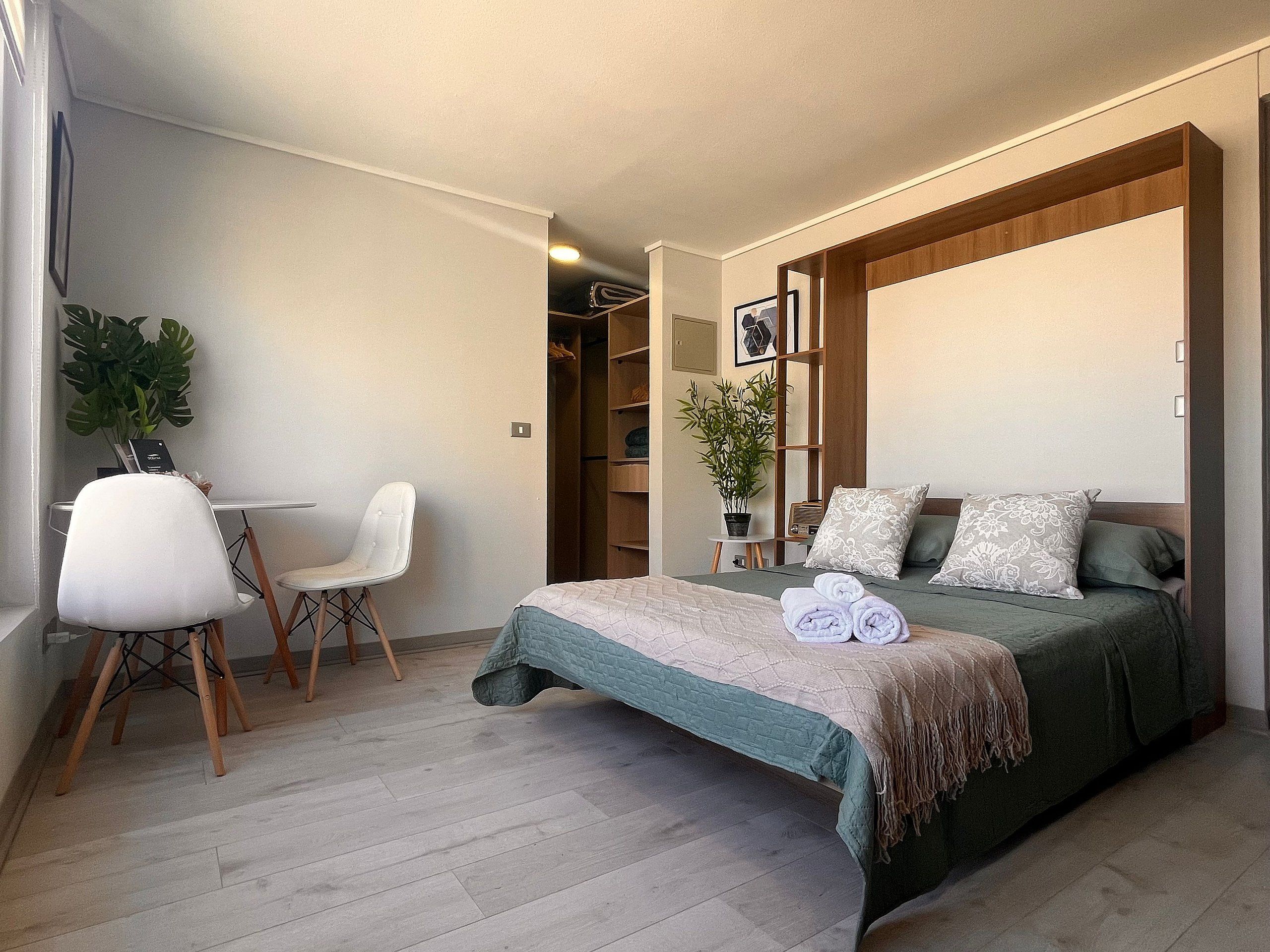 A bedroom with a bed, a chair, a desk, and a plant.