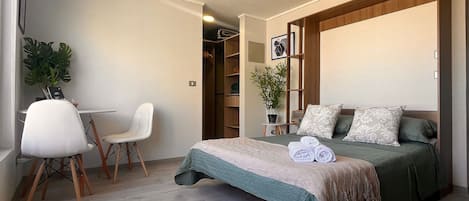 A bedroom with a bed, a chair, a desk, and a plant.