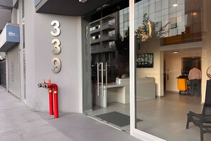 A modern building with the number 339 on the facade, a fire extinguisher, and a glass entrance leading to a reception area. - Oceana Suites Carmen (Santiago)