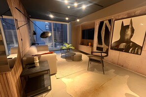 A modern living room with a sofa, a coffee table, and a chair. There is a large window with a view of the city.