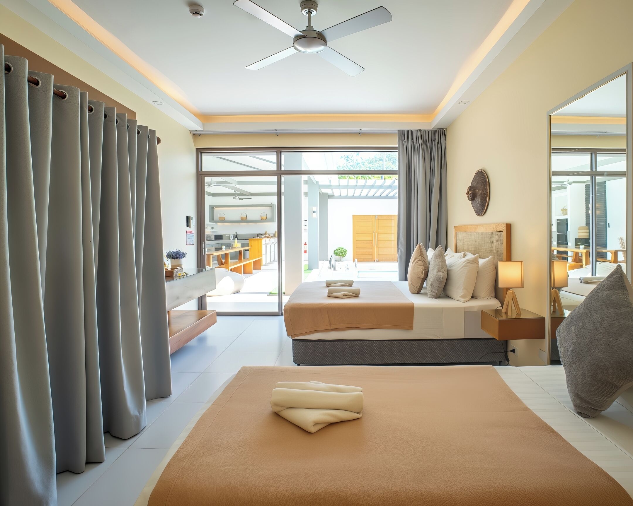 A modern hotel room with a bed, a desk, a chair, a ceiling fan, and a view of the outdoor area.