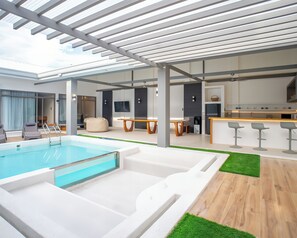 A modern indoor pool area with a glass ceiling, a bar area, and a seating area with a table and chairs. - Villa Kalachuchi Bohol (Panglao)