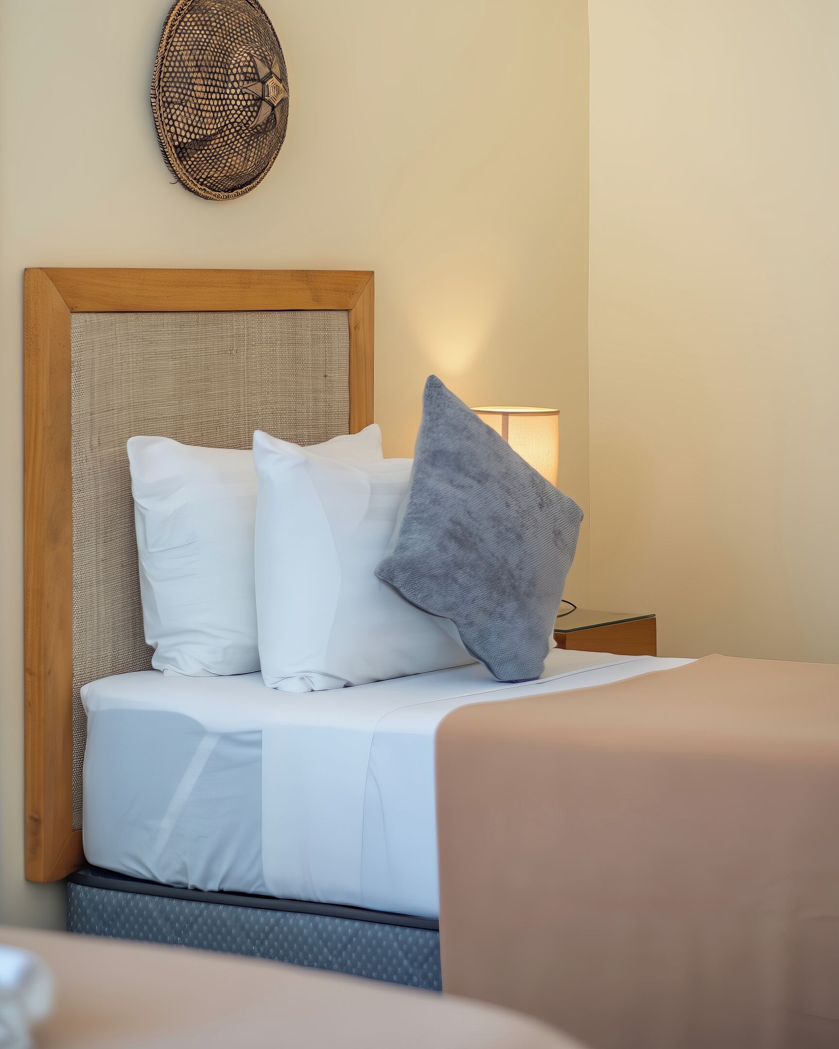 Una cama bien hecha con almohadas blancas y grises, cabecera de madera y un tapiz tejido.