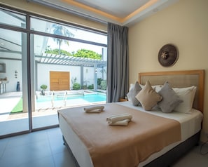 A hotel room with a large bed, a view of a swimming pool, and a patio area. - Villa Kalachuchi Bohol (Panglao)