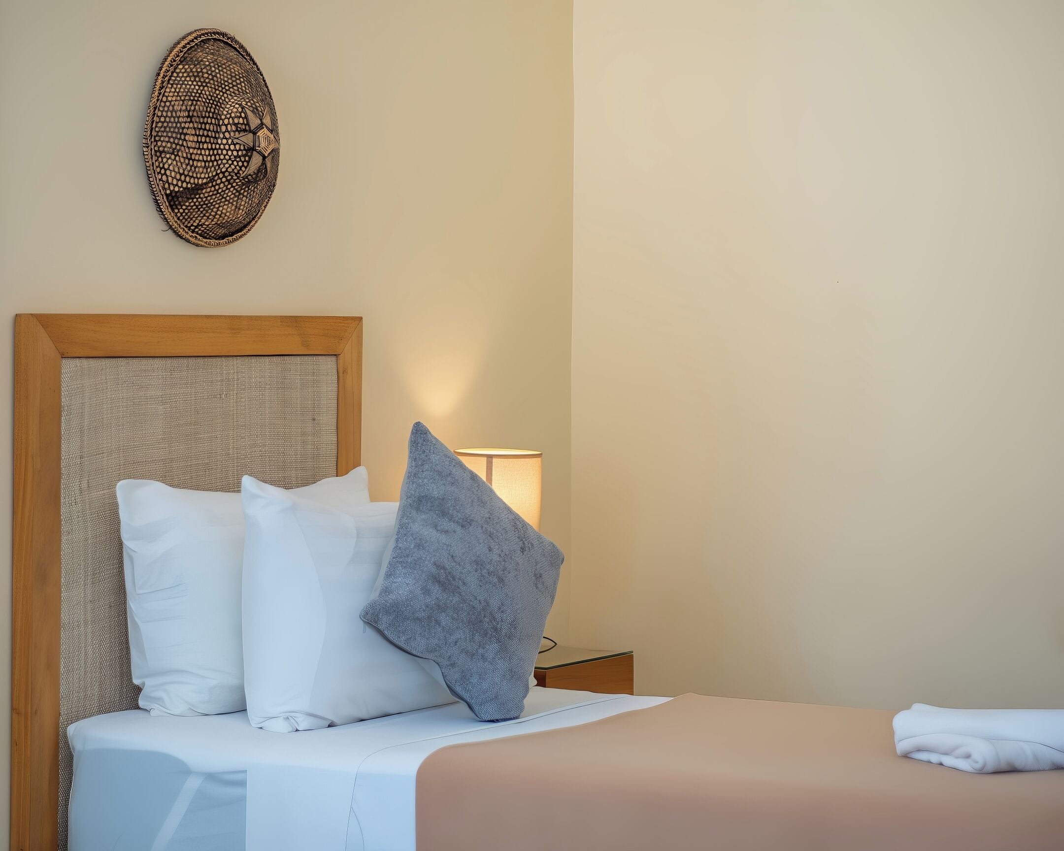 Een net opgemaakt bed met witte en grijze kussens, een houten hoofdbord en een decoratief object aan de muur.