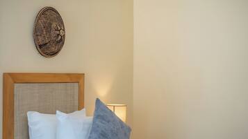 Een net opgemaakt bed met witte en grijze kussens, een houten hoofdbord en een decoratief object aan de muur.