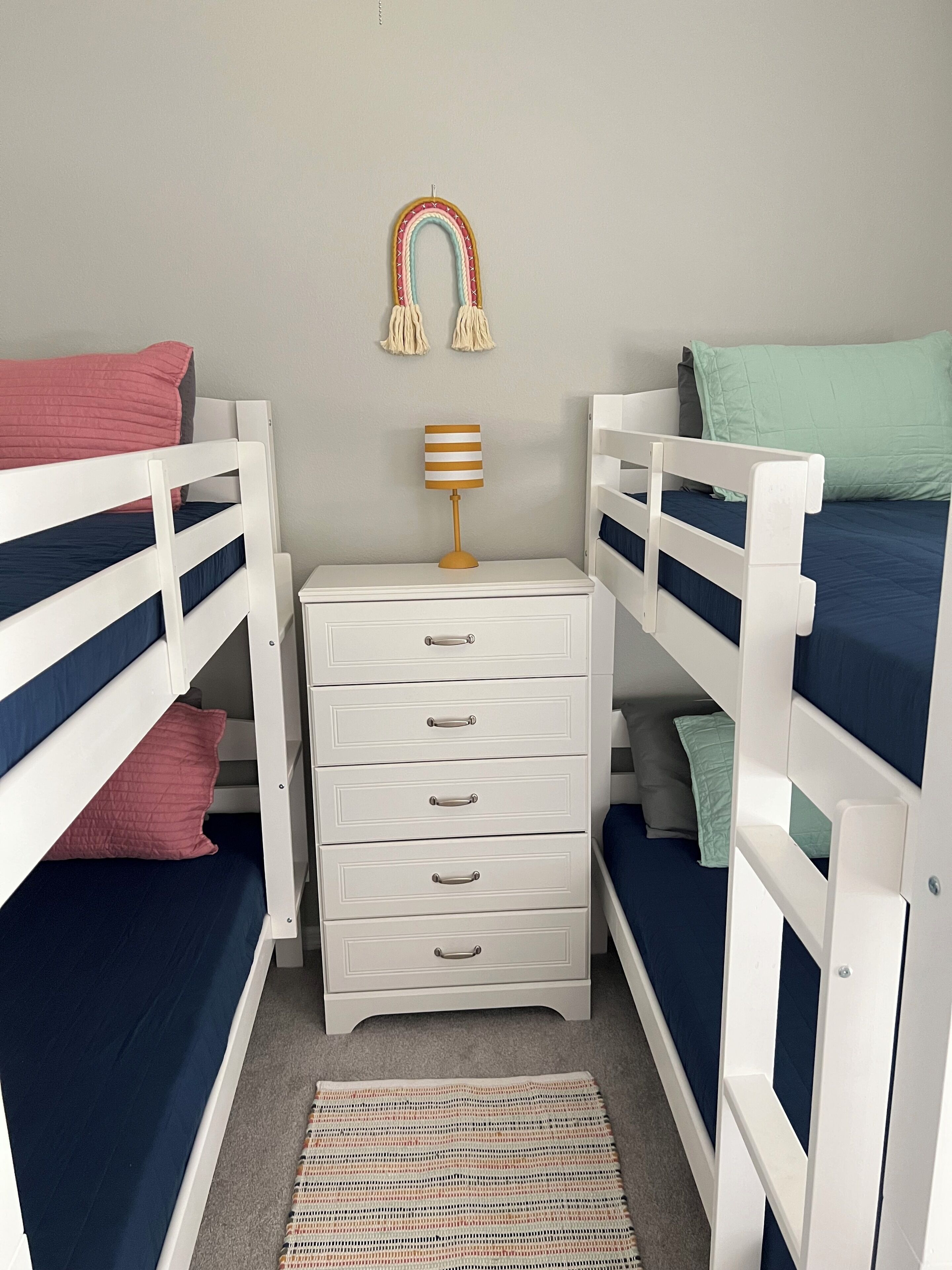 Una habitación infantil con literas, un aparador blanco y una lámpara a rayas.