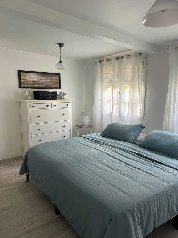 Un dormitorio con una cama, una mesita de noche, una lámpara, un aparador y un cuadro en la pared.