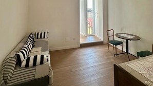 A room with a wooden ceiling, a sofa with striped cushions, a small table with a chair, and a view through an open door. - La Romantique Napoli, 2 minutes from the largest square in Naples (Napoli)
