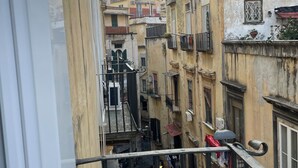 A narrow street between buildings with balconies, a yellow building with a red roof, and a yellow car parked on the street. - La Romantique Napoli, 2 minutes from the largest square in Naples (Napoli)
