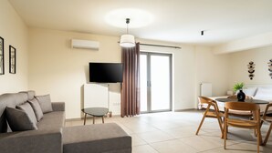 Una sala moderna con un sofá, una mesa de comedor con sillas, un televisor y un gran ventanal corredera.