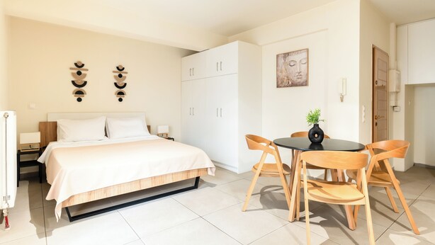 Un dormitorio con cama, mesitas de noche, armario, una mesa de comedor con sillas y una obra de arte colgada en la pared.