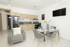 Une cuisine moderne avec des meubles en bois clair, un réfrigérateur en acier inoxydable et un téléviseur à écran plat fixé au mur.